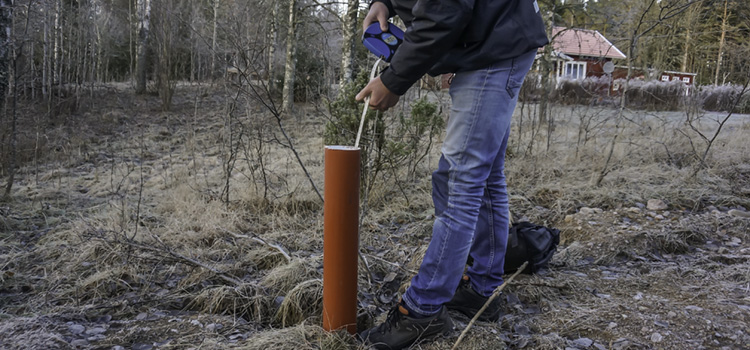 Bilden visar en person som med ett speciellt måttband  mäter hur djupt ner i röret som grundvattnet finns.