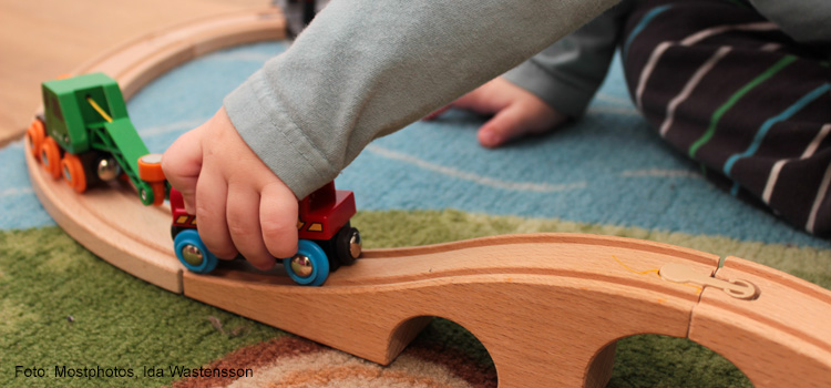 Bilden visar handen på ett barn som leker med ett leksakståg.