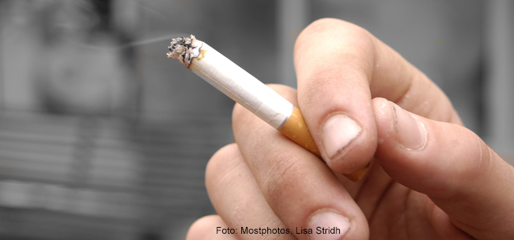 Bilden visar en hand som håller i en tänd cigarett.