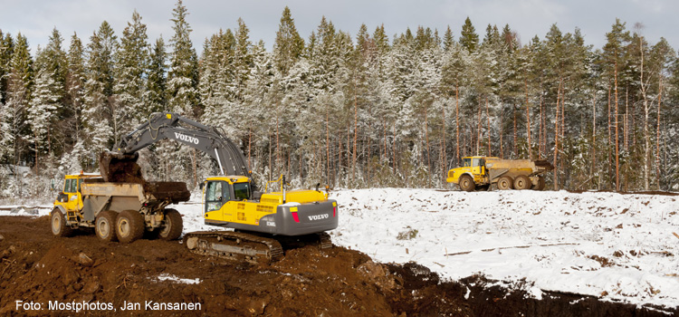 En grävmaskin lastar uppschaktade jordmassor på en dumper.