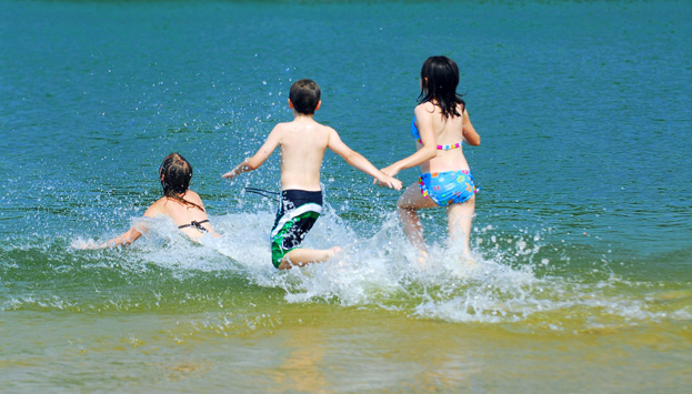 Tre barn som springer ut i vattnet.